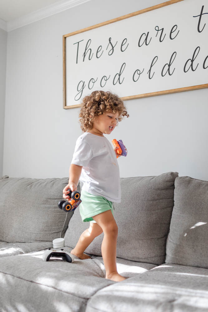 Toddler boy walking on sofa with his cars