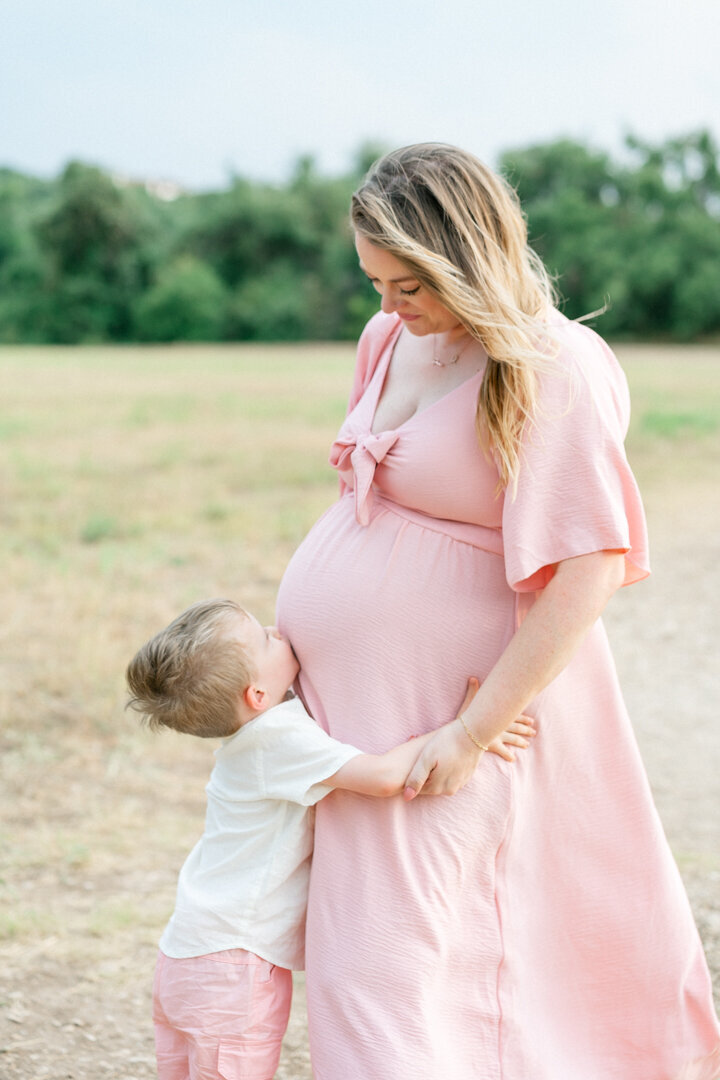 a toddler boy kisses his pregnant mother's belly during their maternity session in Cedar Park. 