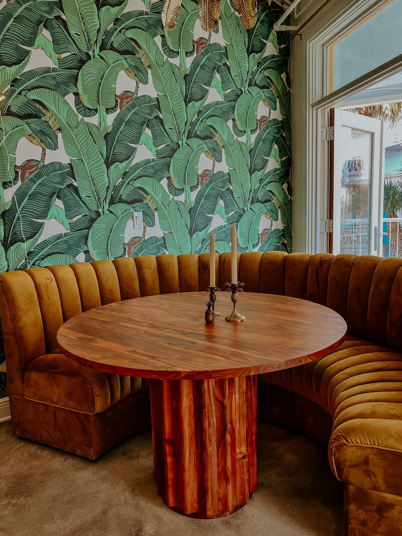 round velvet corner booth with wooden table and palm leaf wallpaper