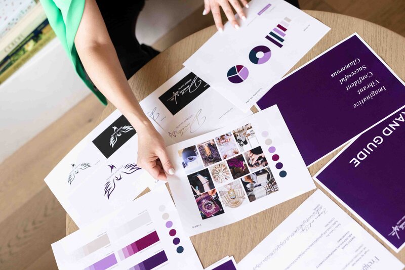 Brand strategy presentation featuring mood board with purple color palette, custom logo designs and curated client photography laid out on wooden desk