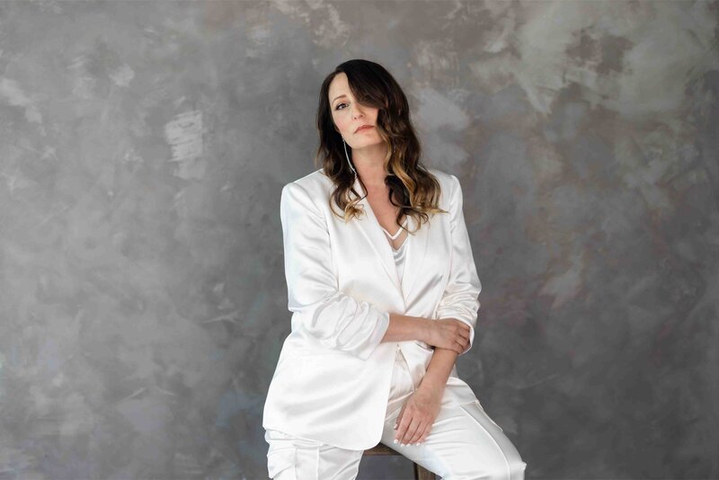 Brand strategist in luxurious white silk blazer posing confidently against textured grey backdrop during professional brand photoshoot