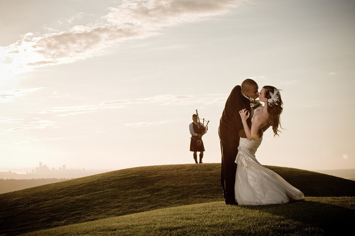 Groom dips bride and kisses her next to man playing bagpipes