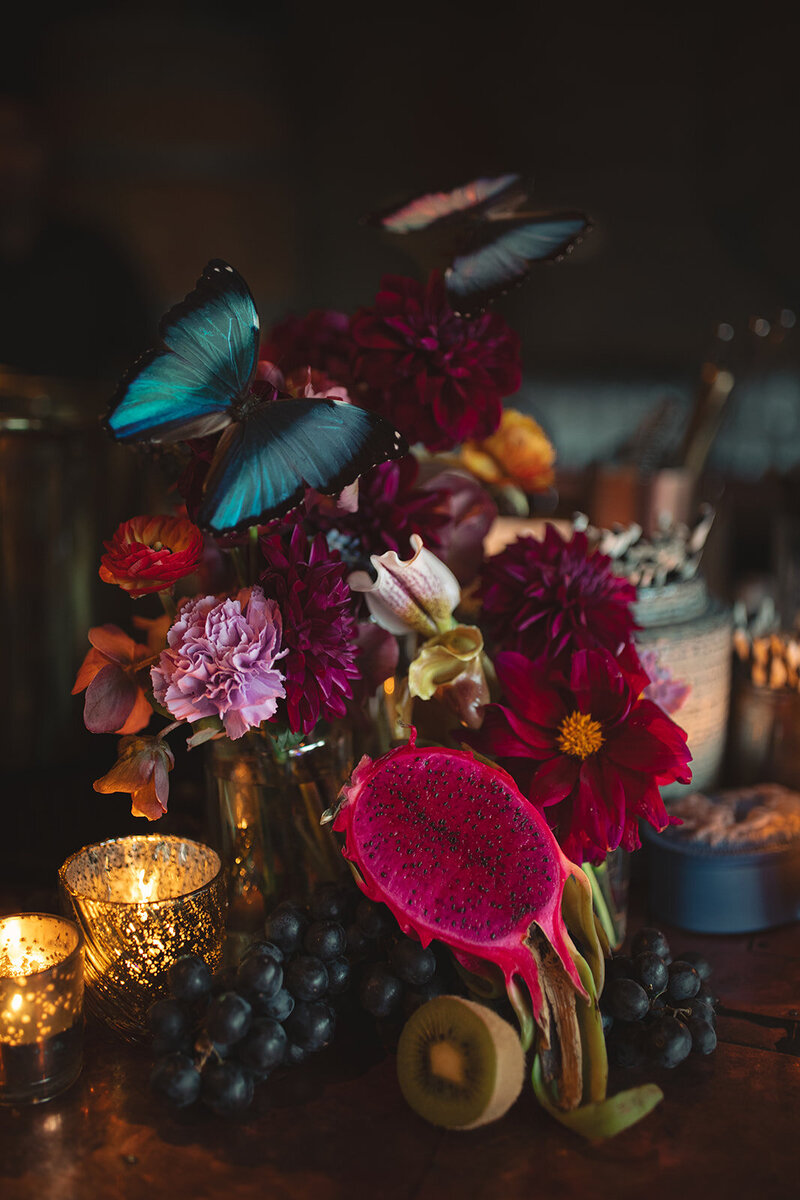 a moody floral, fruit, and butterfly still life tablescape centerpiece