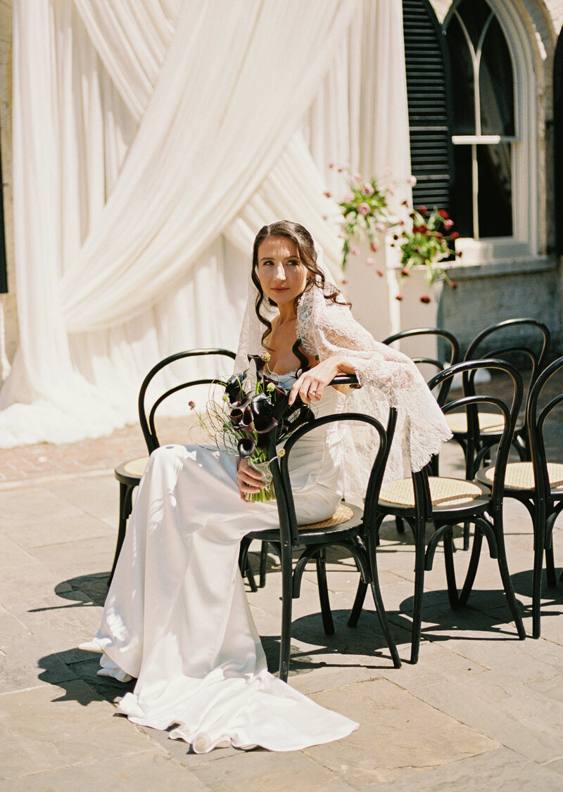 a bride sitting on ceremony chairs holding her bouquet 