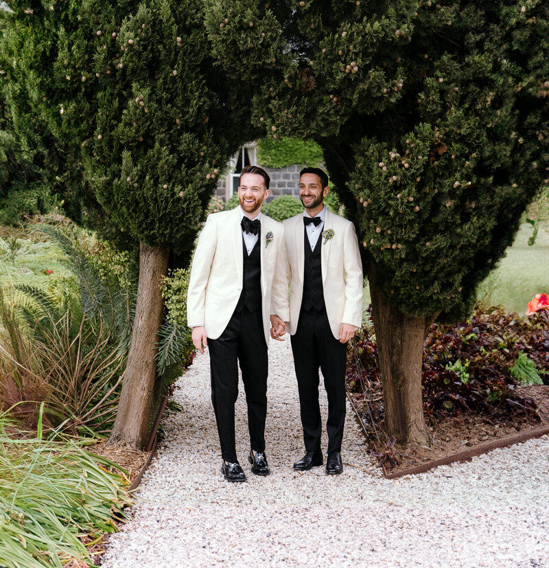 A gay couple in matching suits hold hands in a posed wedding photo