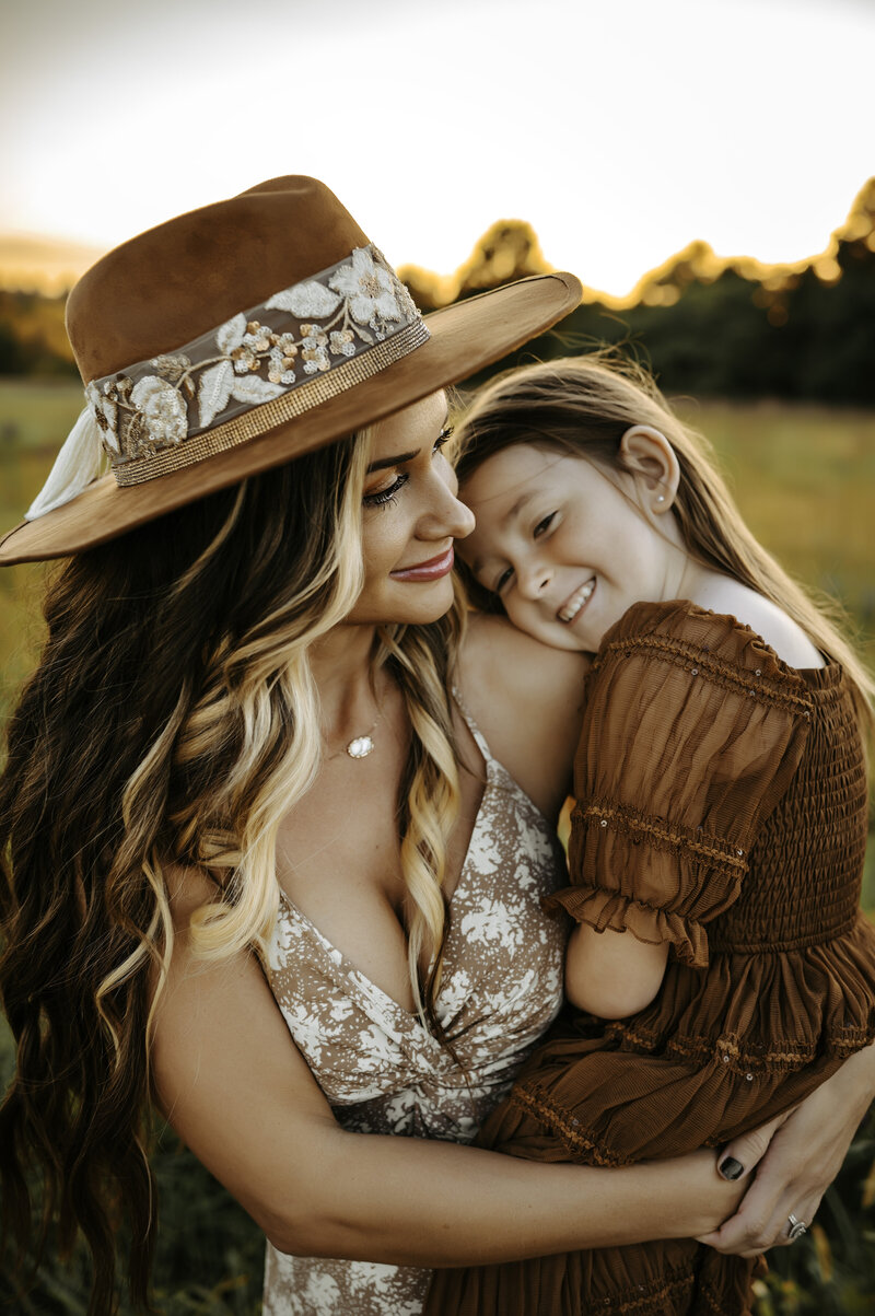 Mom snuggling her daughter at sunset