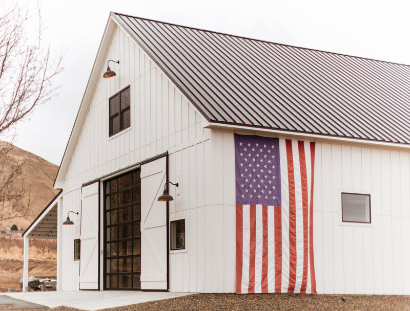 Side of white barn with large American flag hanging down.