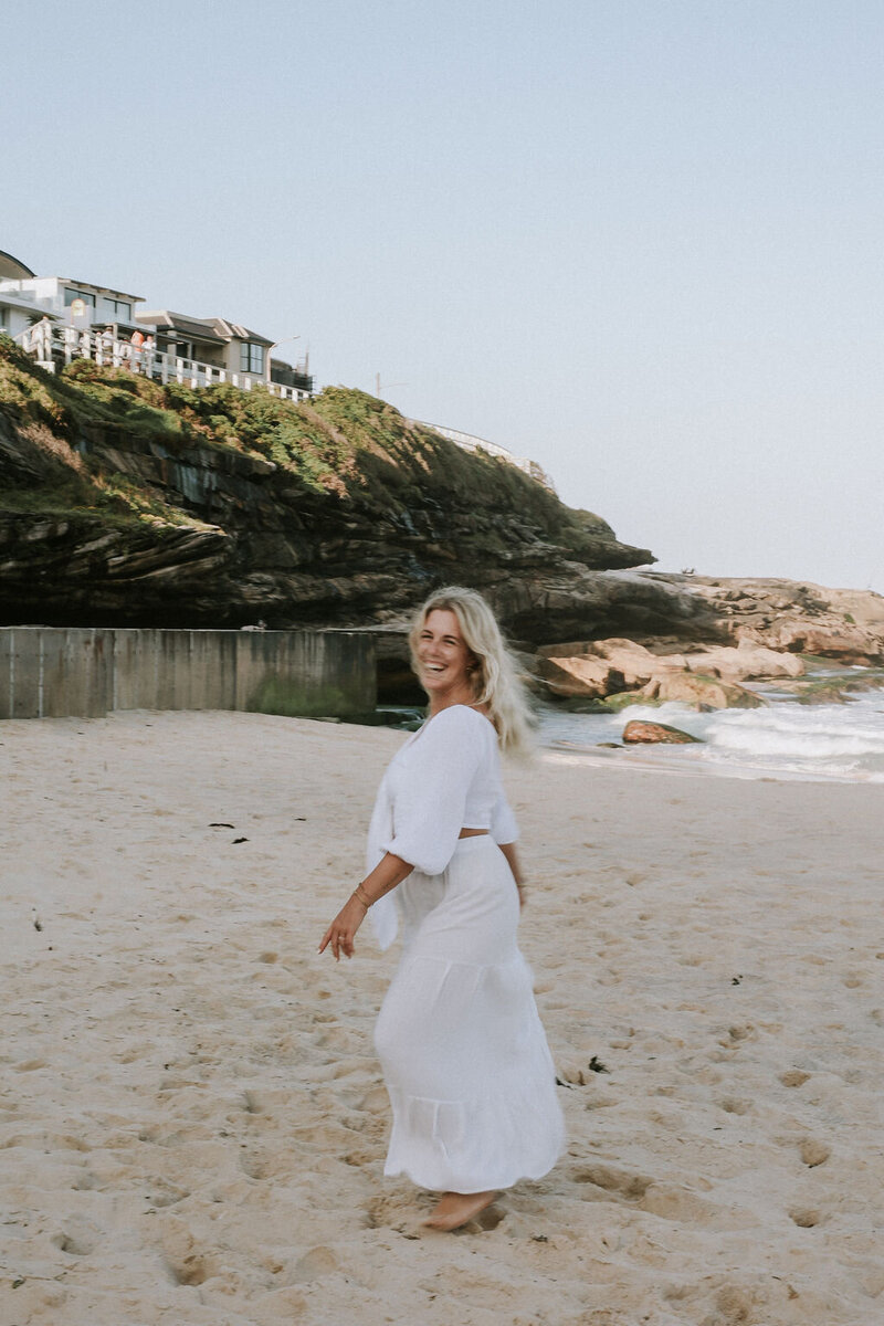Women in white dress smiling and walking on a beach surrounded by cliffs