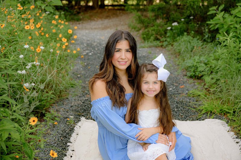 daughter dressed in white sits in her mothers lap during their mommy and me mini session