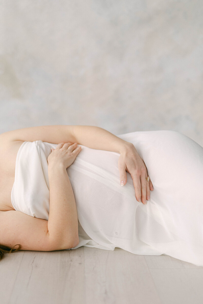 pregnant women draped in fabric laying on floor in front of painted fine art backdrop holding belly knoxville tennessee newborn photographer