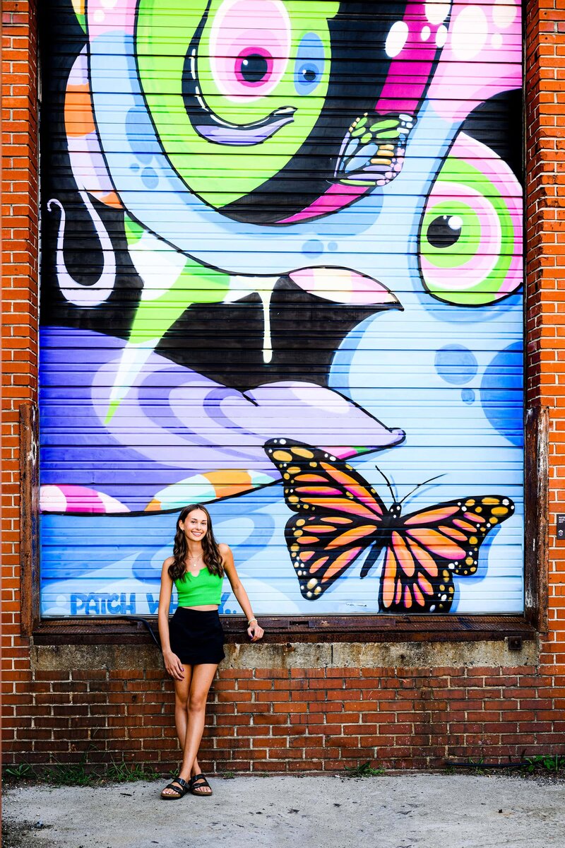 decorative graffiti wall shot of senior wearing green top and black shorts with neon above her