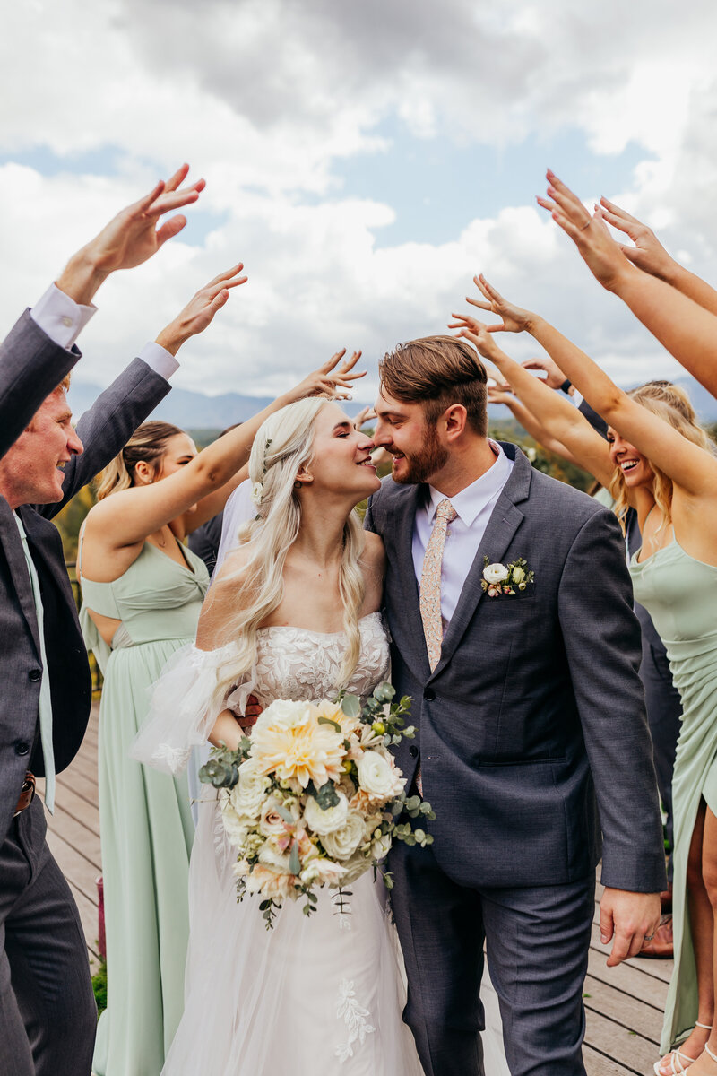 bride and groom almost kiss while surrounded by celebratory wedding party