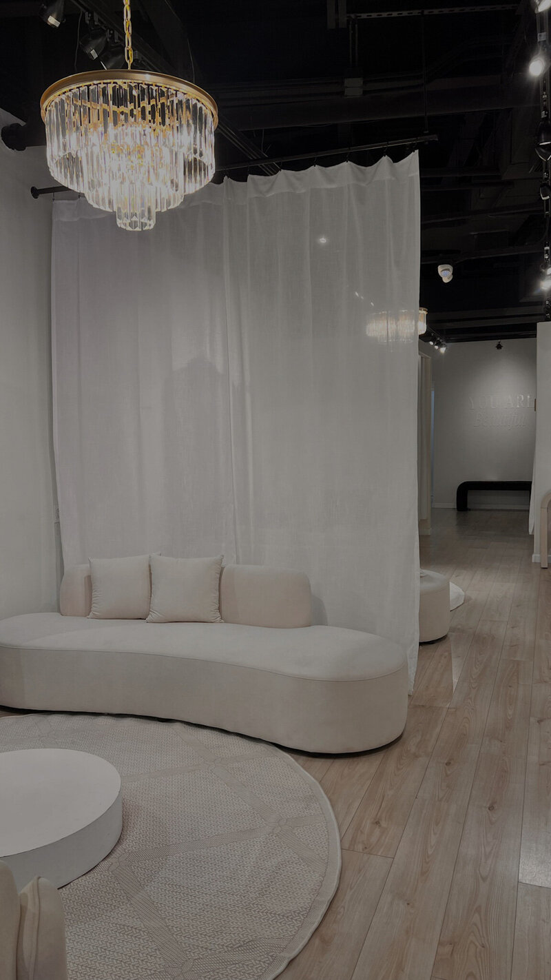 J Bridal Boutique inside shop of the seating area lounge with plush sofa, sheer curtains separating the stages and romantic chandeliers 
