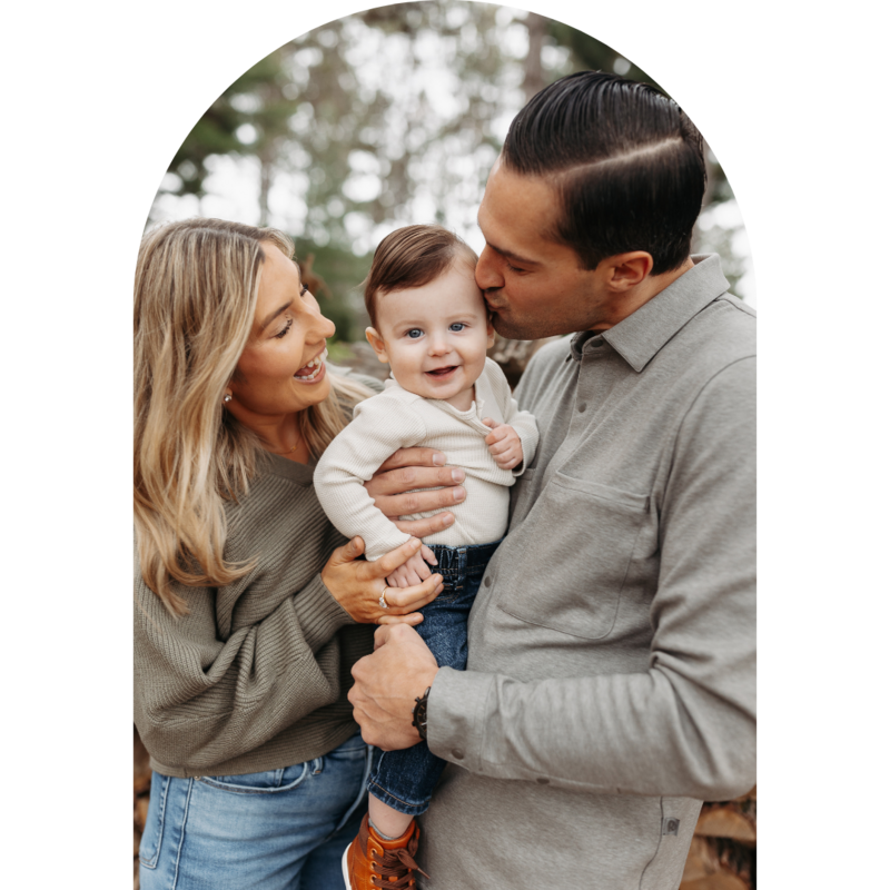Man and Woman holding baby and man kissing the side of baby's face