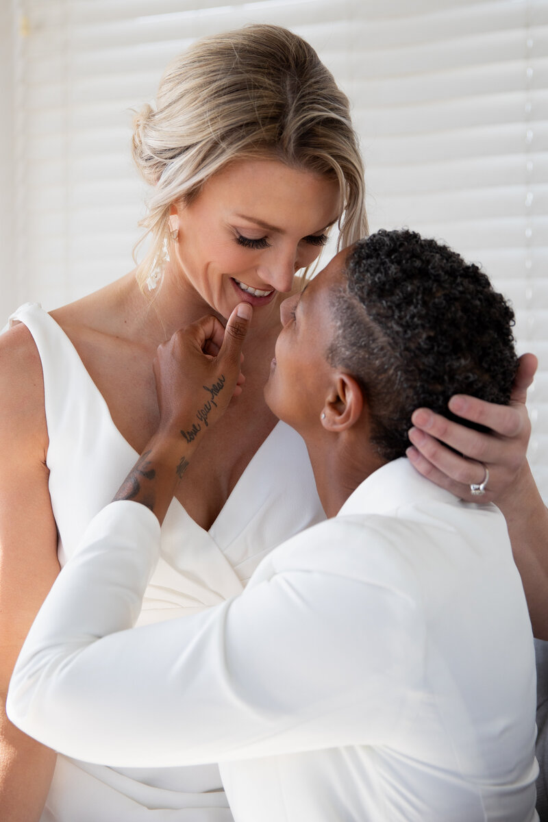 Elopement Wedding Packages Rhode Island | Kelsey Sheehan Photography Timeless Rhode Island Weddings | A loving couple embraces closely, both in white attire. One partner gently touches the other's face, sharing a tender, intimate moment, both smiling softly.