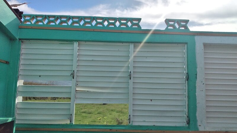 Storm-damaged classroom wall with broken shutters and missing panels after Hurricane Melissa.