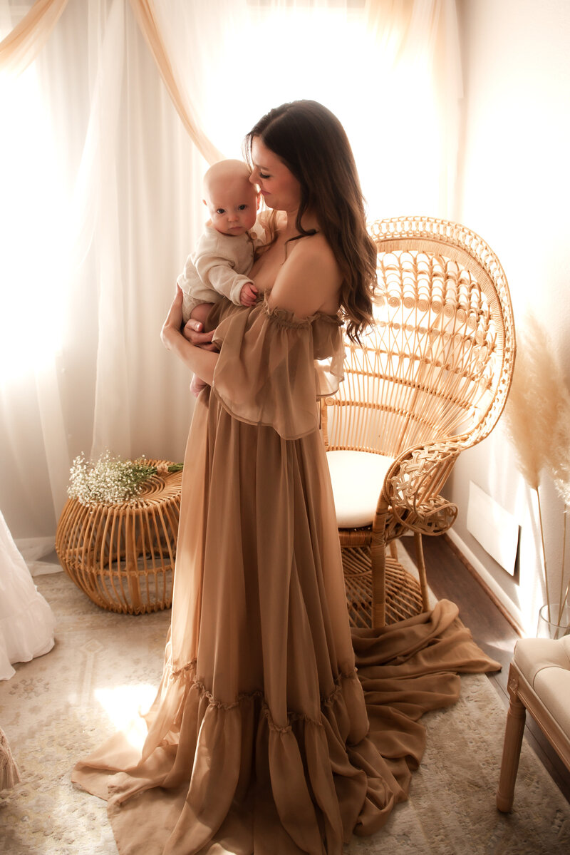 Mother holding her baby in Hope's in home studio wearing one of her beautiful client closet gowns.