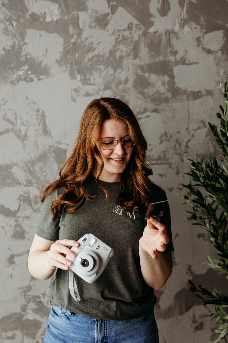 Photo of woman holding a polaroid camera and polaroid photo smiling.