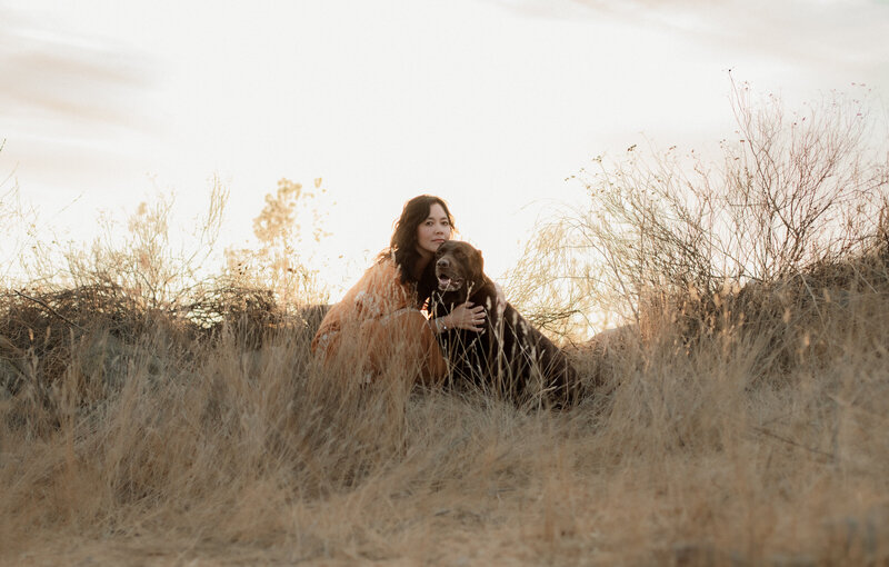 Outdoor portrait of a woman and her chocolate Labrador, both looking at the camera, taken in Menifee, California.