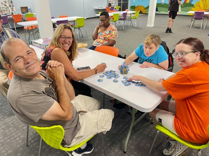 Friends sitting at table smiling and playing board game at Solid Rock's Adult Day Program.