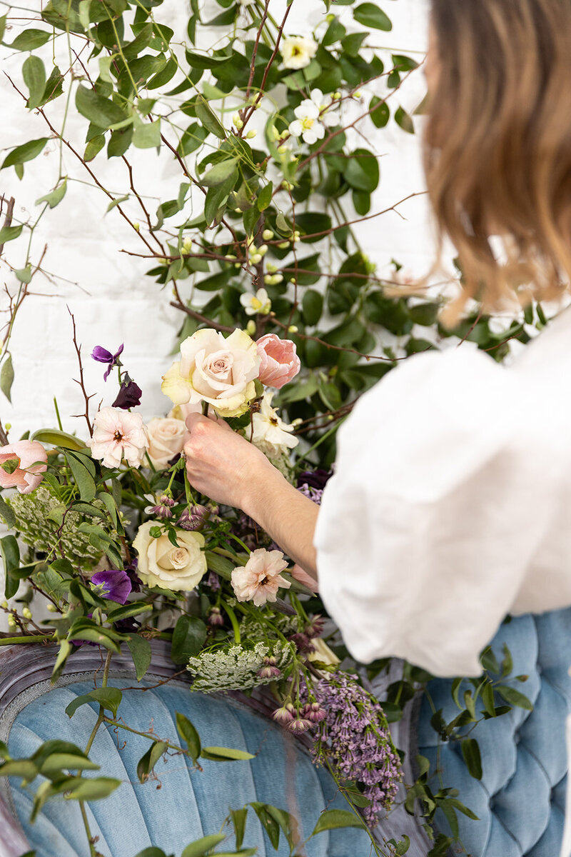 A woman reaching to adjust flowers in a large flower display, her back is to the camera