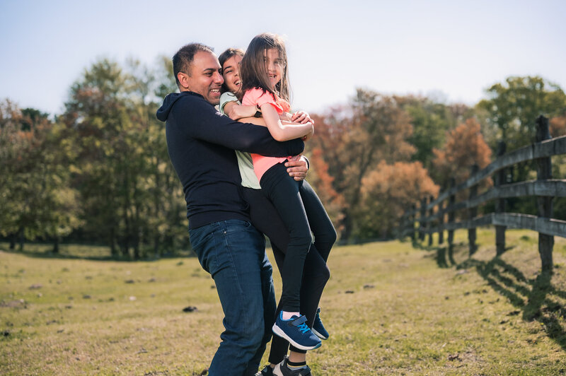 Dad playing hugging lifting two daughters in a field on a local farm