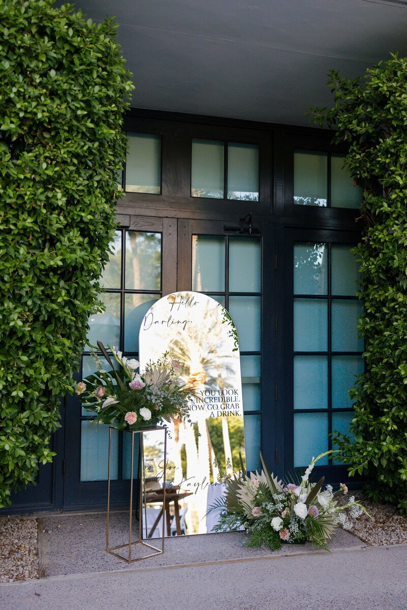 Large mirror serves as welcome sign for wedding guests and is styled with large tropical floral arrangements.
