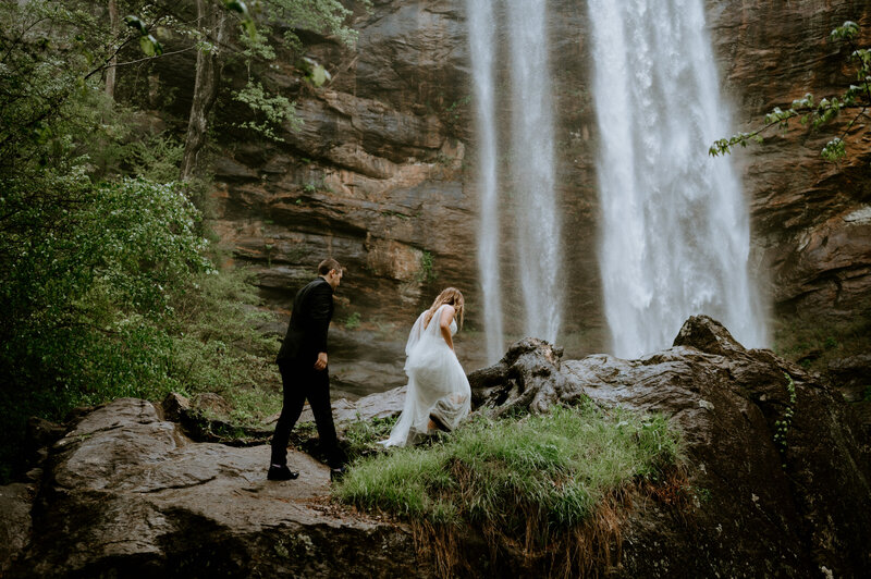 An elopement couple walks up a hill in front of a massive waterfall.