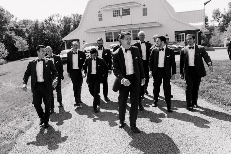Black and white photo of a groom and his groomsmen in front of the WIldflower On Watts white barn venue