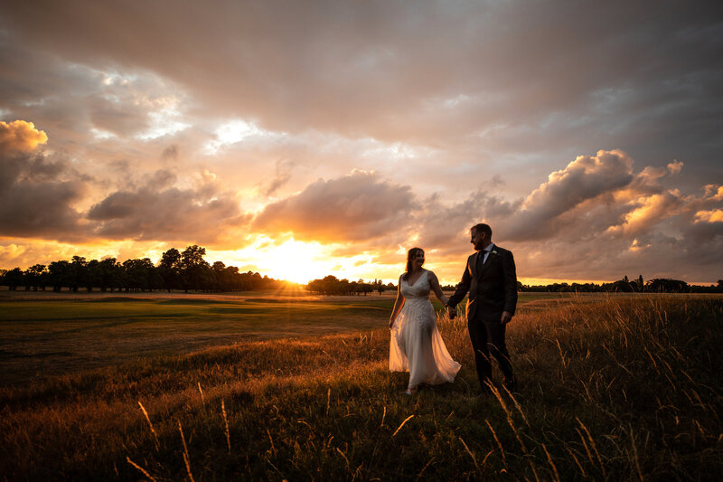 Bride and groom walking together at sunset in countryside