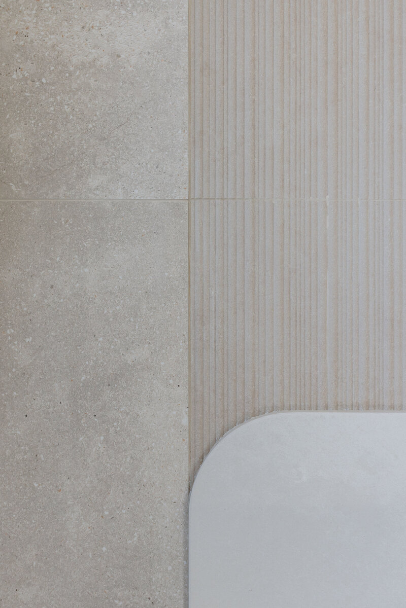 Close-up of light beige textured tiles with linear grooves next to smooth rectangular tiles with rounded edge, showcasing the elegance that a Newcastle Kitchen and Bathroom Designer can bring to your space.