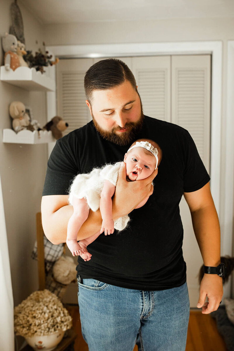 dad with blue eyes in an olive green henley holding his swaddled baby boy in harrisburg newborn photos