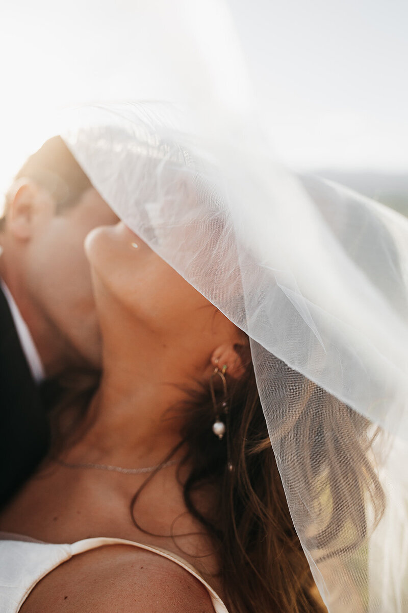 Photo of groom kissing bride with her veil over her face