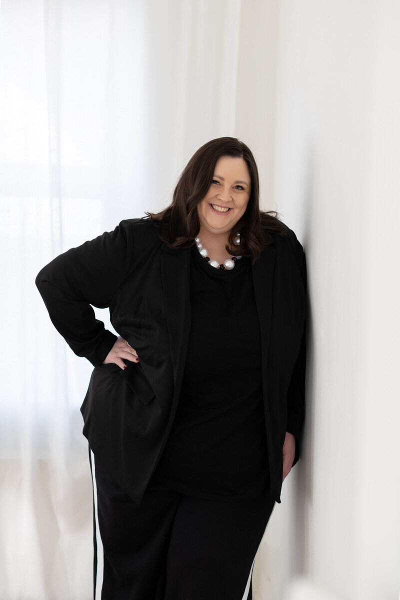 Professional headshot of luxury brand designer Sarah Shuttle in black blazer and pearls.