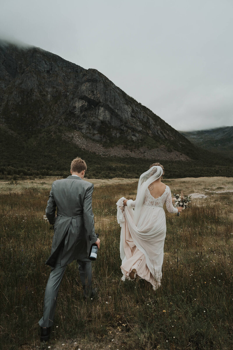 Wedding couple walking in a field of flowers with a big mountain behind them in Senja, Norway