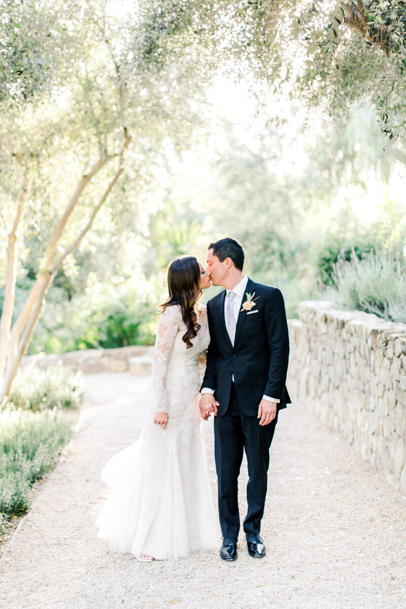 Bride and groom kiss while walking down a stone path