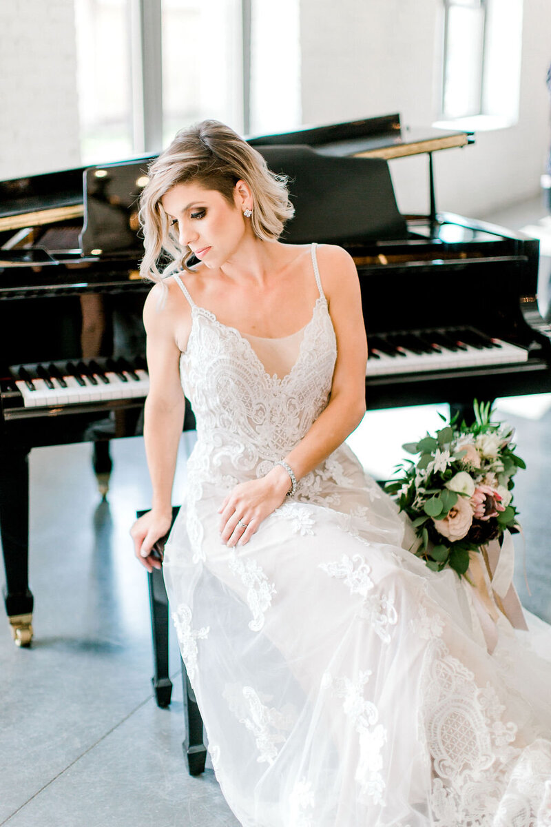bride sitting by the piano holding flowers and looking don