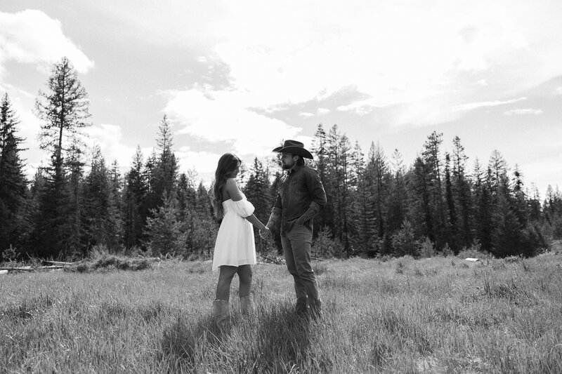 a couple standing in an opening forest field looking at each other