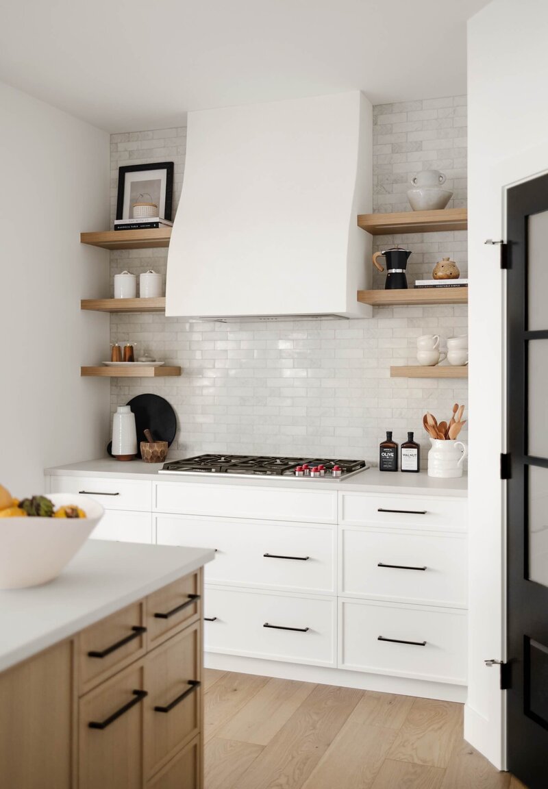A modern farmhouse kitchen with plaster hoodfan, white oak open shelving and black accents paired with subway tile. 