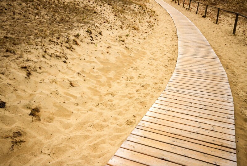 A boardwalk  path on sand  with a black fence to the right.