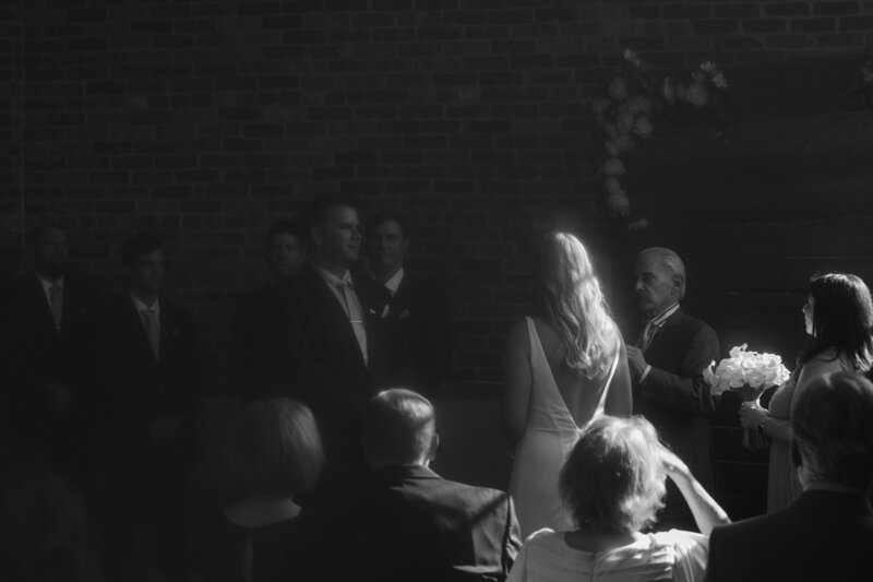 Black-and-white photo of a bride illuminated by a spotlight during her wedding ceremony in Denver, Colorado, capturing a moment of pure elegance