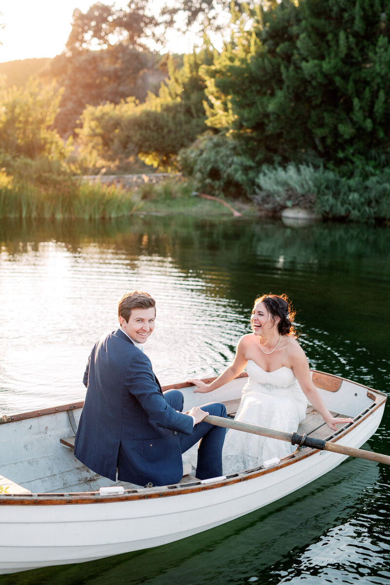 Bride and groom laugh in rowboat on the water on their wedding day