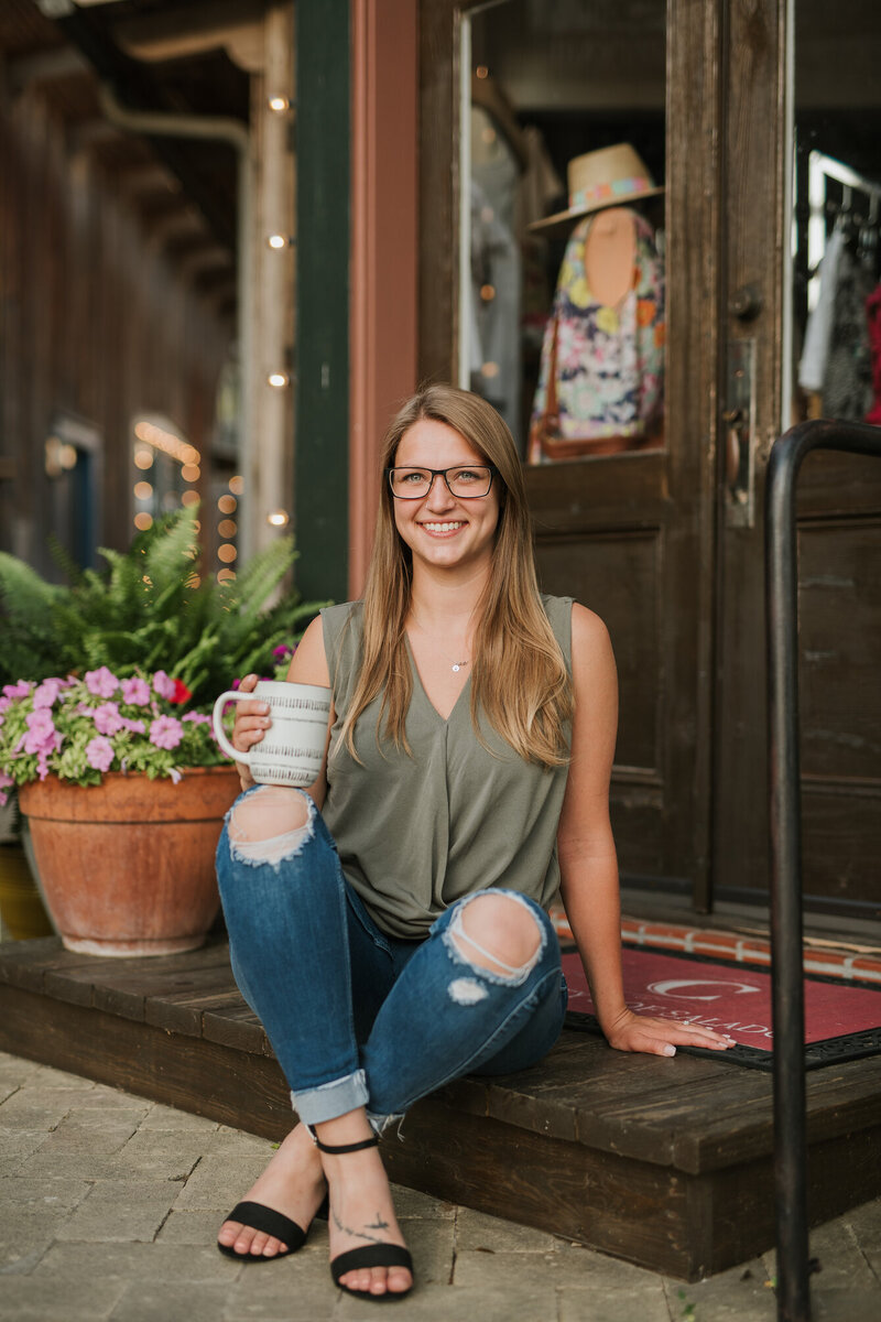 Shawna sitting down holding a cup of coffee and smiling at the camera