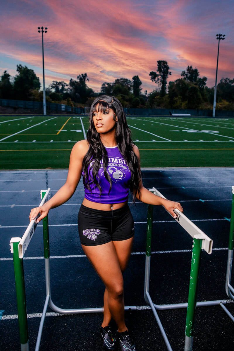A powerful portrait of a Black female track runner at Columbia College, standing between hurdles with a breathtaking sunset backdrop. A dynamic and inspiring image of athleticism and grace