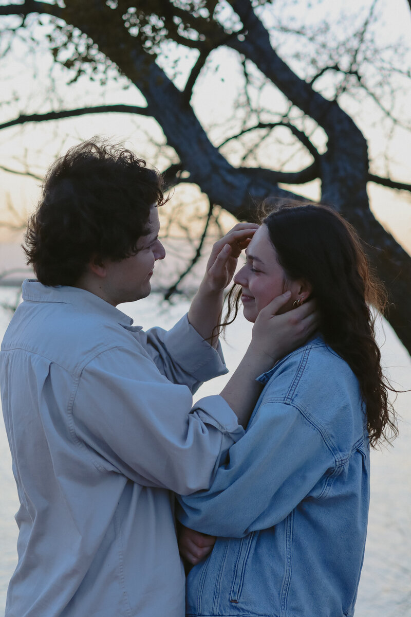 A man can be seen tucking hair behind his wife's ear that has flown in from of her face due to the wind. They are smiling at each other.