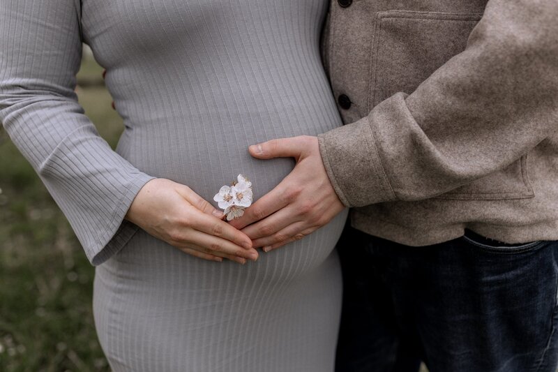 Mann und Frau halten Babybauch und Blume