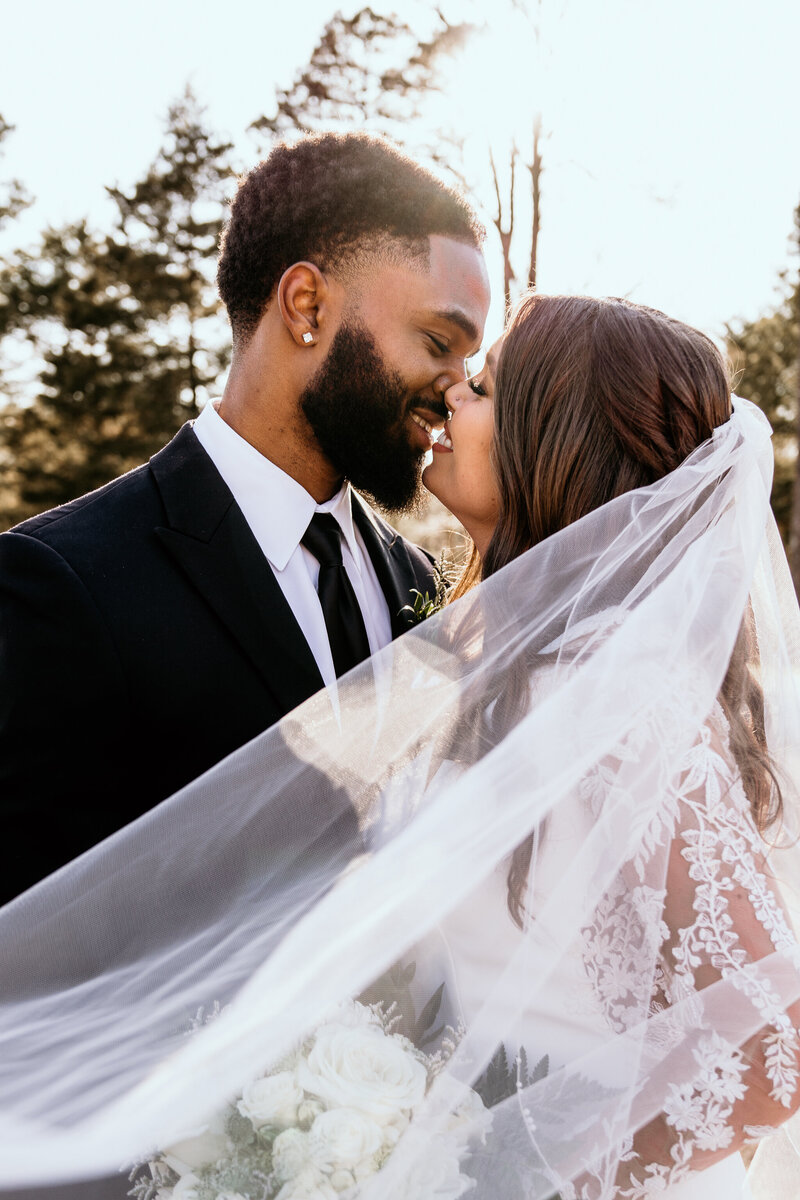 The bride and groom lean in for a kiss with the brides veil draped across the image at sunset