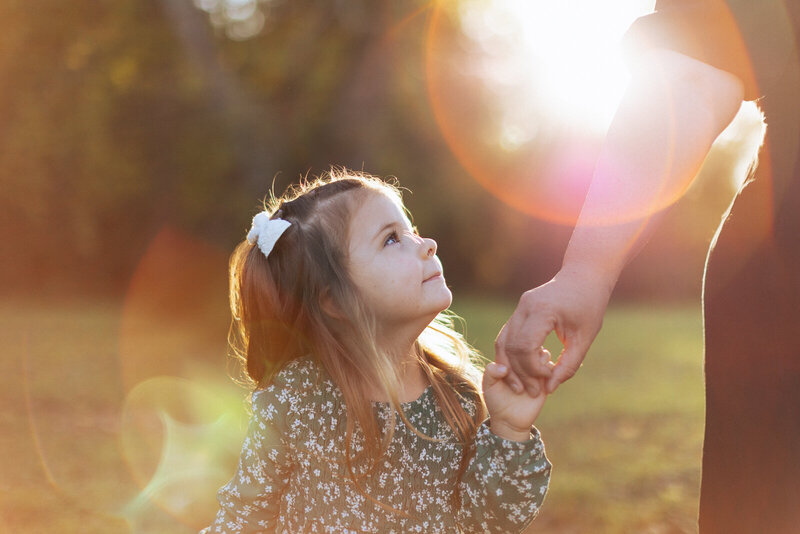 Close up portrait at sunset of a girl holding her mom's hand and looking up at mom. 