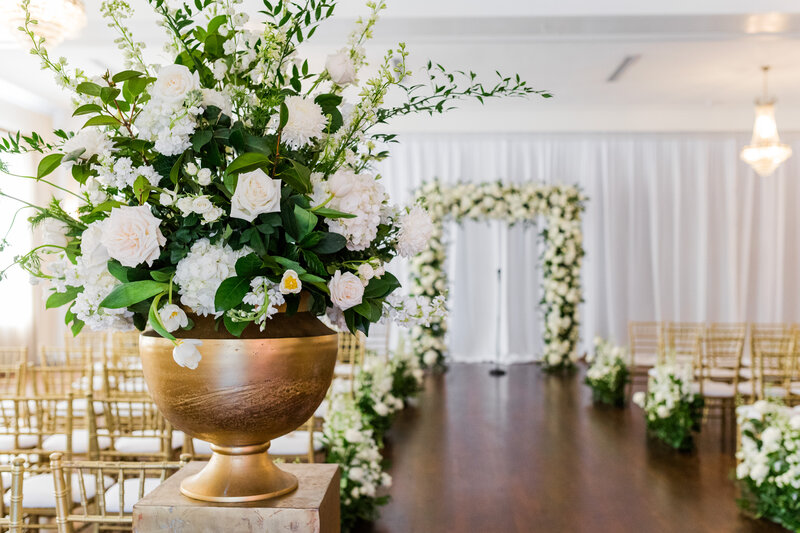 Wedding ceremony space at The Orlo in Tampa Fl is set up with beautiful green and white flowers in gold vases with gold chairs for guests