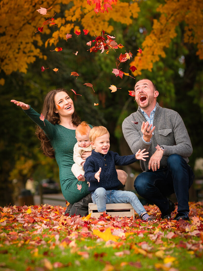 Family of four throws colorful red leaves in the air during an autumn family portrait session